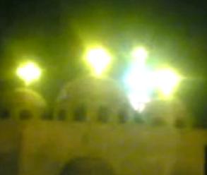 photograph of the apparition of the Theotokos at Warraq al-Hadar, 11 December 2009: the luminous figure of the Virgin Mary above the central dome of the Coptic Orthodox Church of the Virgin Mary and the Archangel Michael, in royal blue belt and crown, with the cross visible above her crown; widely-circulated mobile phone and press photographs are extant from December 2009 onward