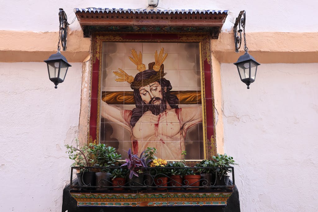 Detailed mosaic of Christ on a wall in Cádiz, Spain, with surrounding plants.